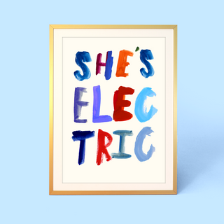 Framed artwork with colorful text 'SHE'S ELECTRIC' on a light blue background